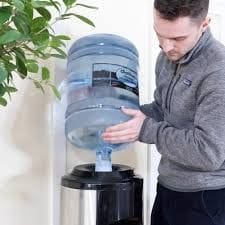 A man is putting water in the top of a water cooler.